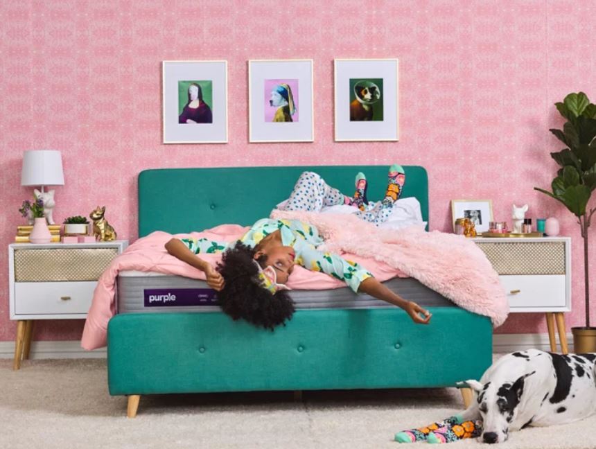 Woman laying on turquoise bed with a purple mattress.