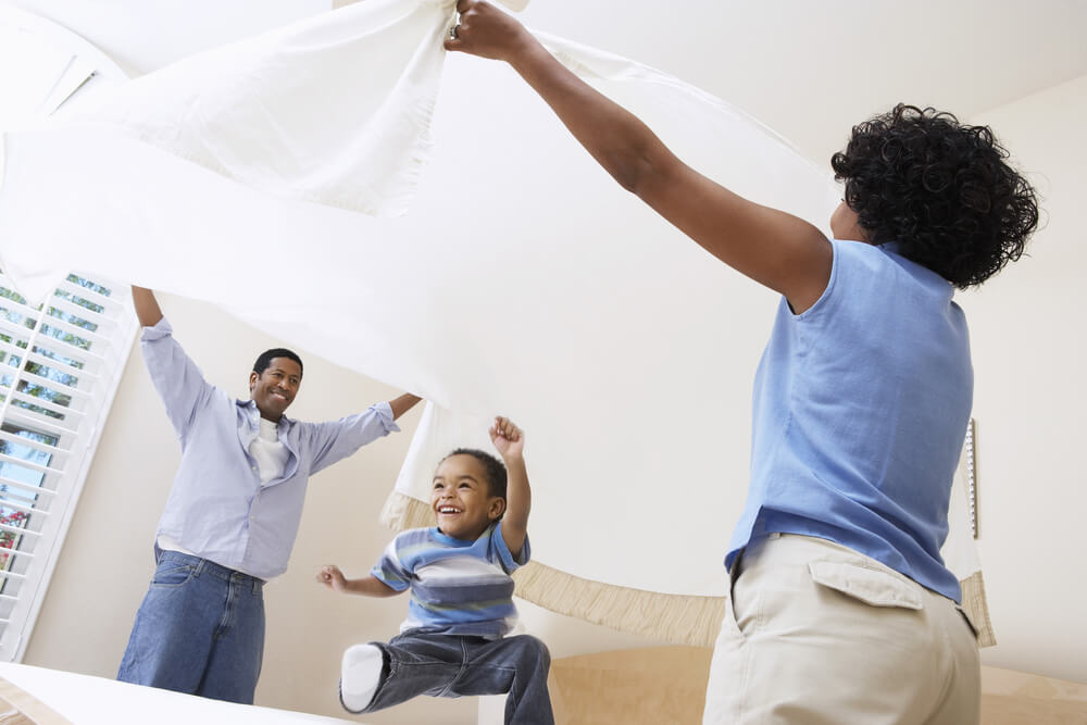 African American parents spreading softened bed sheet over son in bedroom