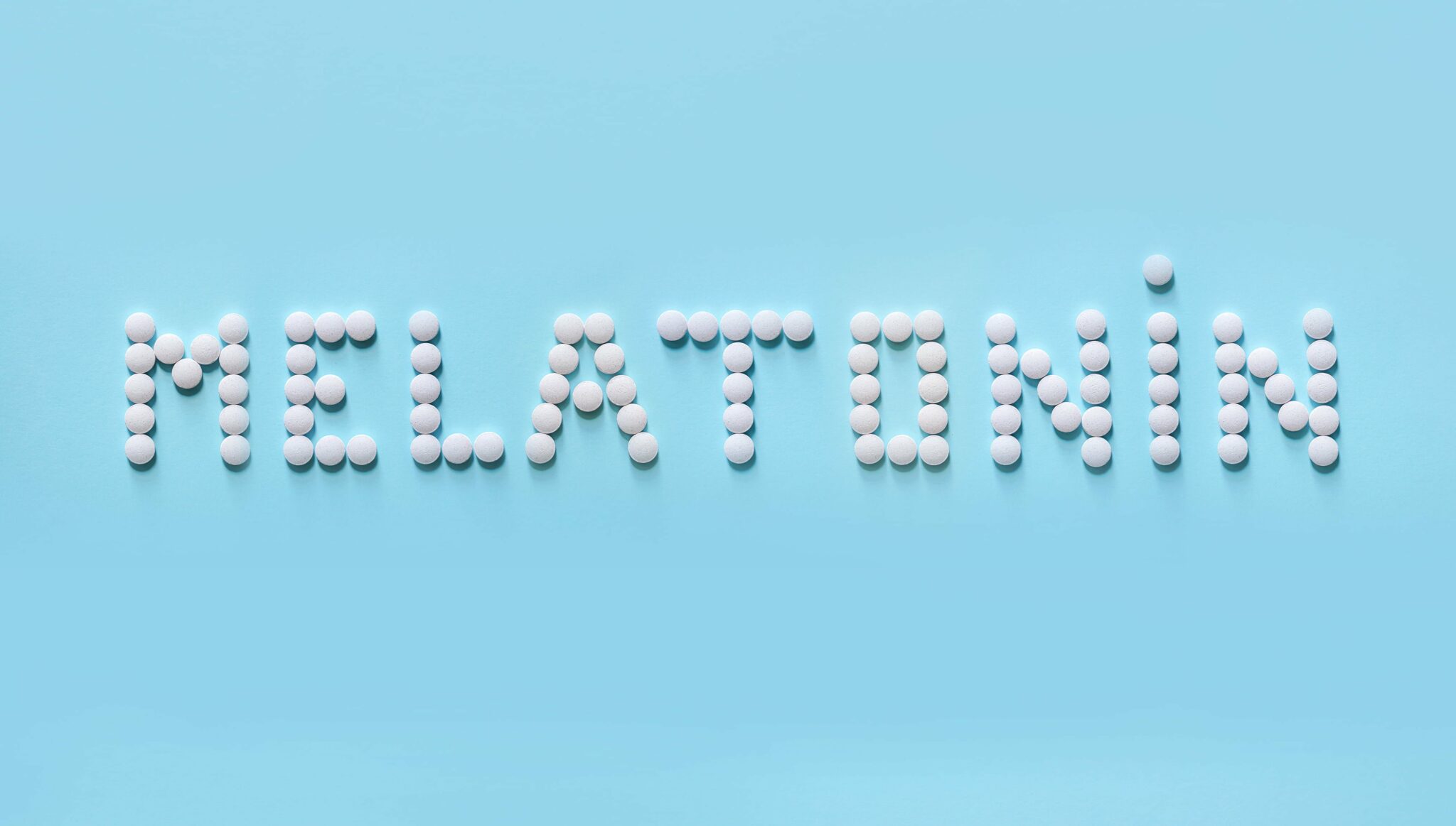 The word "melatonin" spelled with pills against a light blue background.