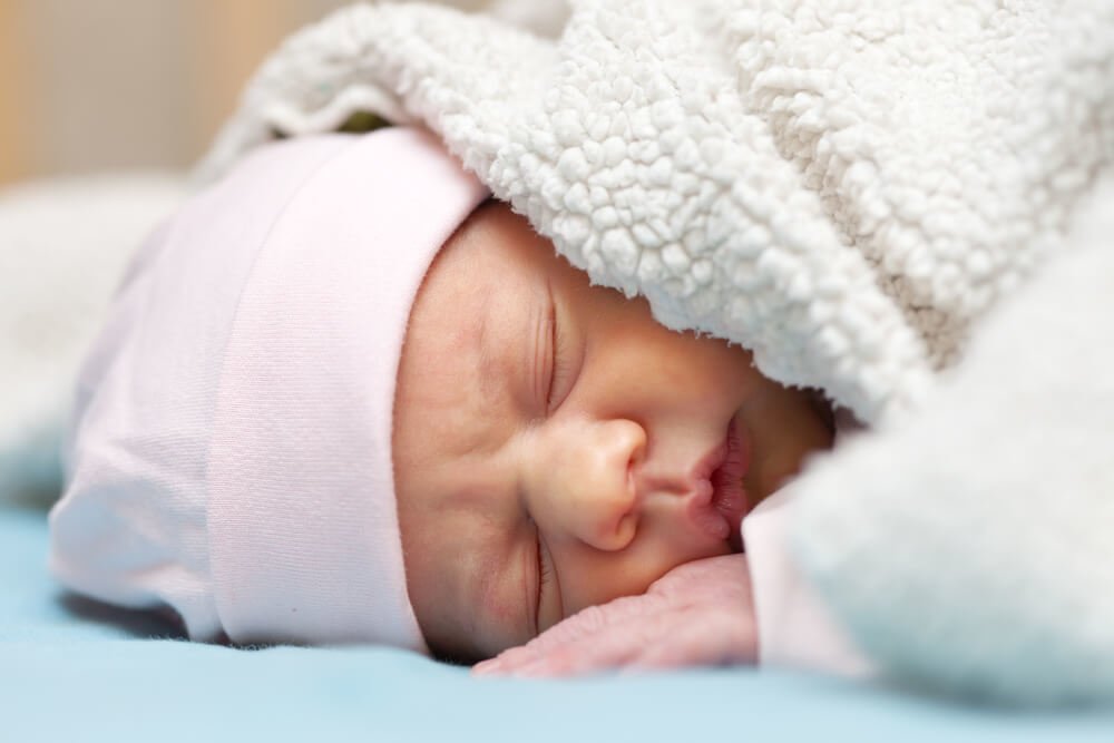 newborn baby sleeps under blanket while sleeping on stomach.