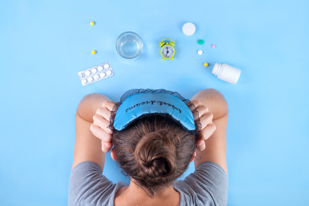 Insomnia concept. Sleep mask, a cure for insomnia, an alarm clock, a glass of water on a blue background. Depression and sleep concept.