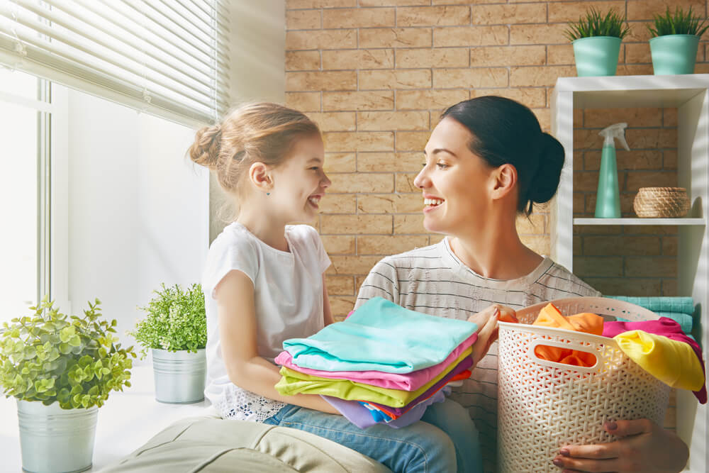 Beautiful young woman and child girl little helper are having fun and smiling while doing laundry at home; how to soften sheets concept.