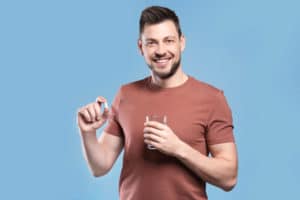 Handsome young man with pill and glass of water on color background; over the counter sleep aid concept art.