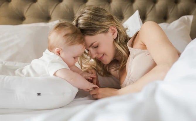 A woman cuddles with her baby on a bed.