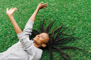 Young girl in gray hoodie and with braided hair lying on grass, smiling, stretching her hands