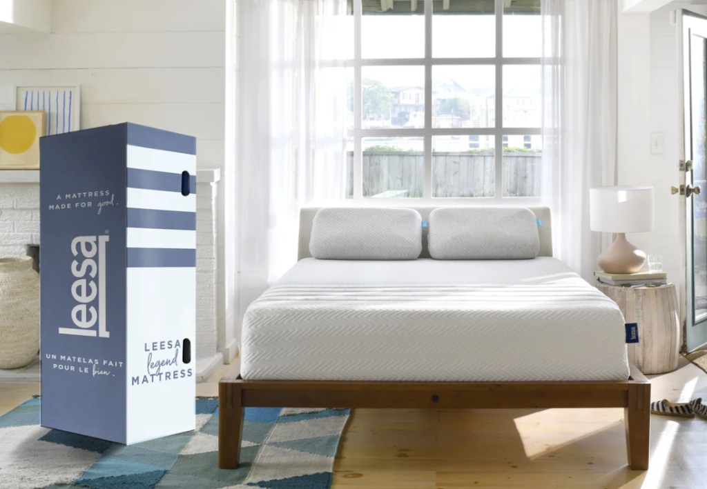 A white Leesa Legend hybrid mattress on a wooden bed frame with a blue and white box.