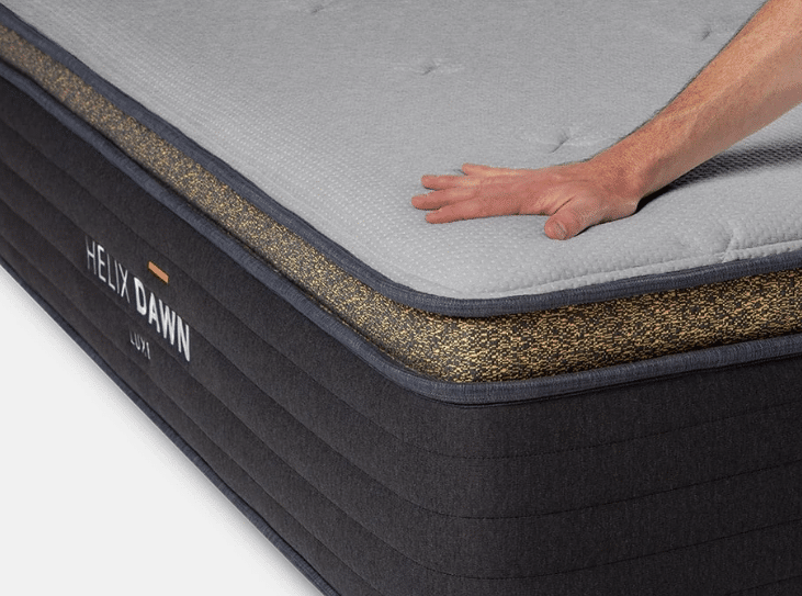 A hand presses on a firm Helix Luxe mattress for stomach sleepers.