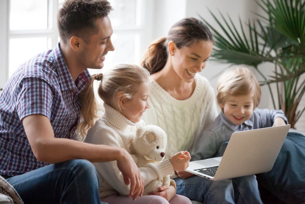 Two parents with two kids looking at a laptop and smiling.