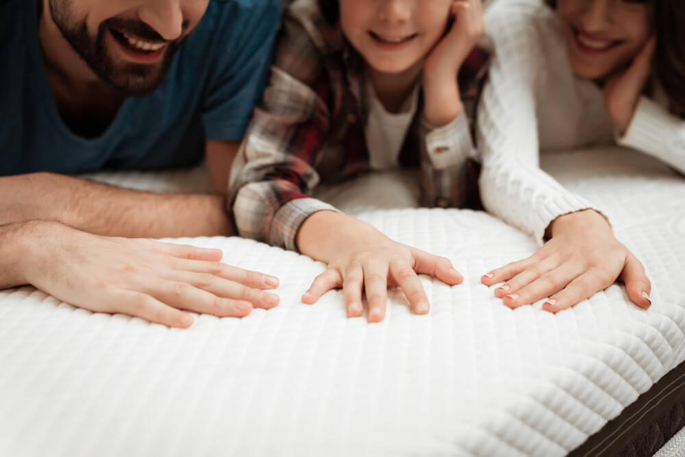 A couple with their daughter looking at a white mattress.