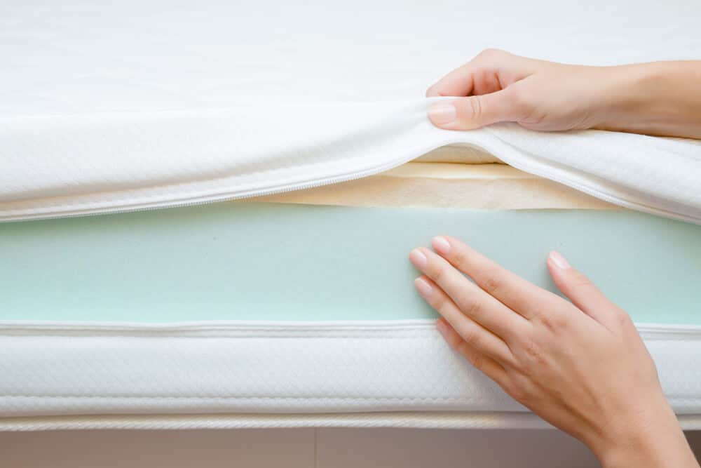 Woman's hands touching different layers of new foam mattress. Checking hardness and softness. Choice of the best type and quality. Front view. Close up.