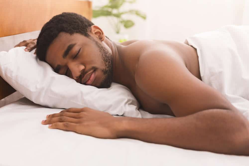 Portrait of african-american man sleeping shirtless on stomach in bed at home, closeup
