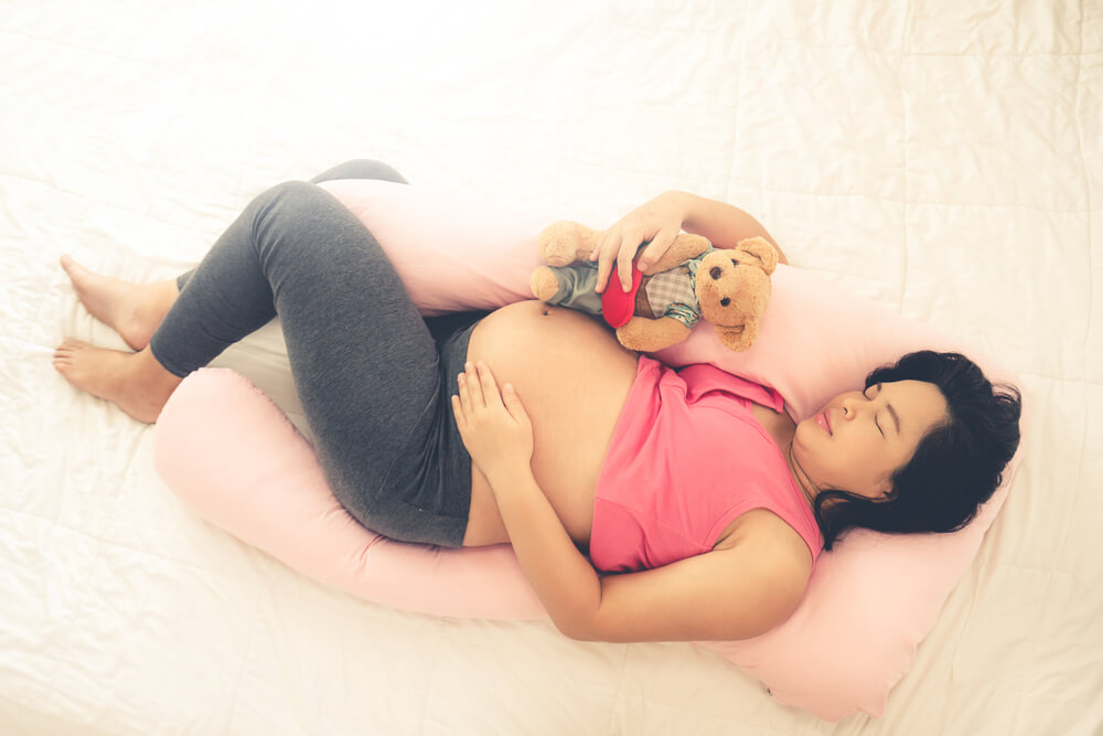 Happy pregnant woman sleeping on bed in bedroom at home for resting and stress relief. The young expecting mother holding baby in pregnant belly. Maternity prenatal care and woman pregnancy concept. B