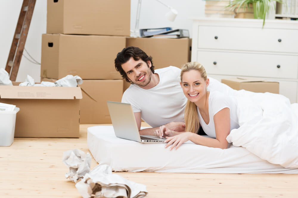 A couple sitting on a mattress with boxes surrounding them.
