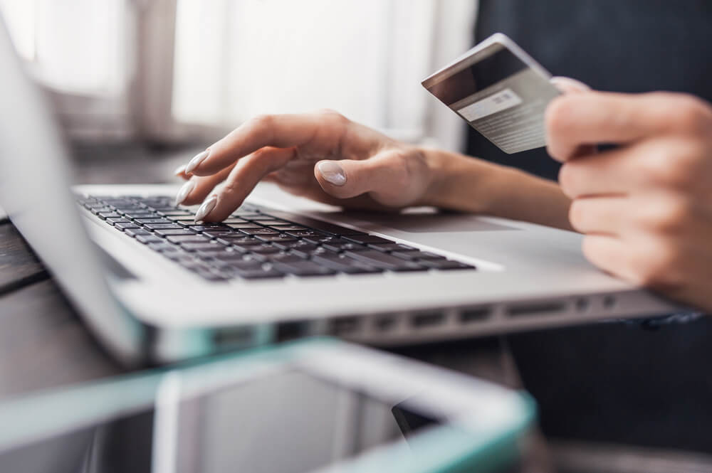 A person typing on a laptop and holding a silver credit card to buy something online.