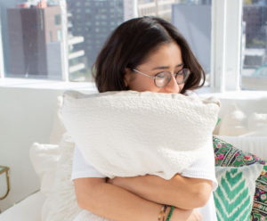 A woman clutching a white pillow and smiling.