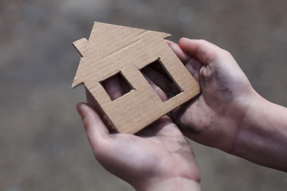 A homeless youth holding a cardboard house with a cut-out window and door.