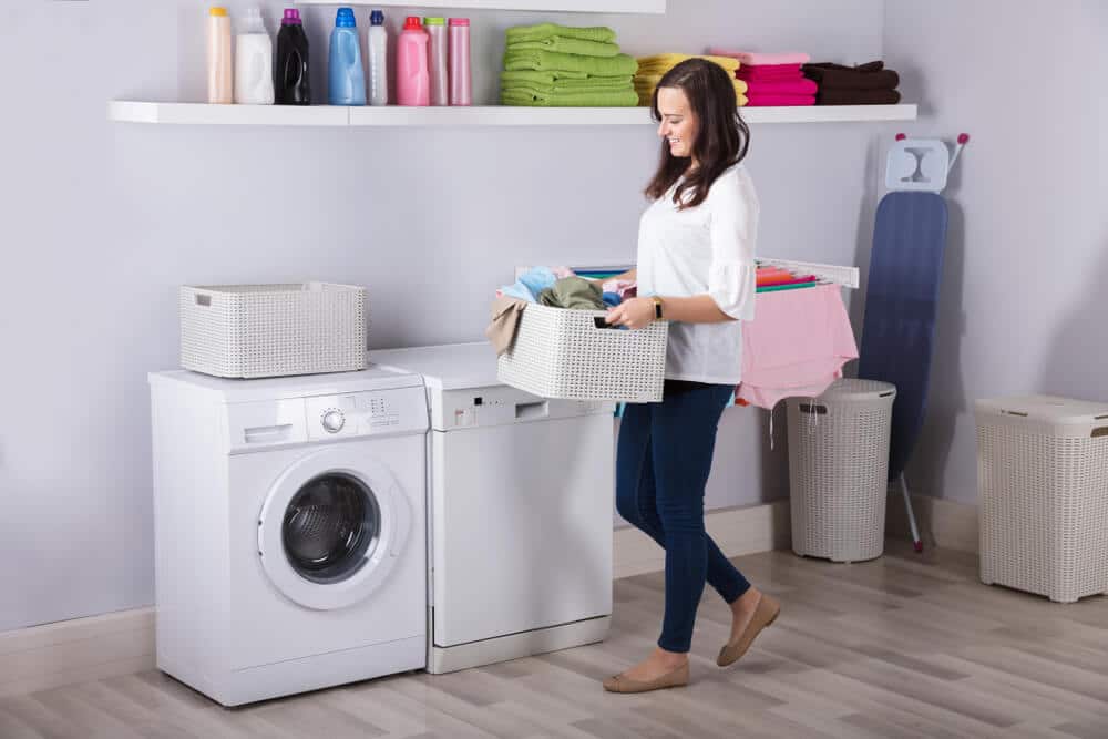 A woman carries a load of laundry to her washing machine.