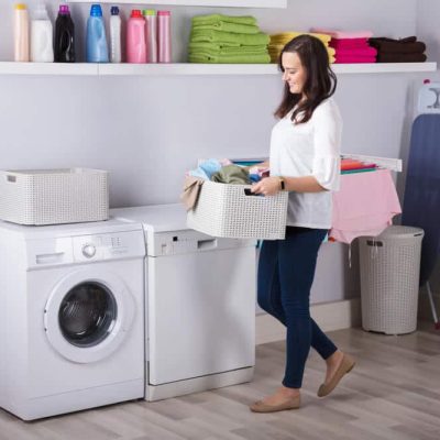 A woman carries a load of laundry to her washing machine.