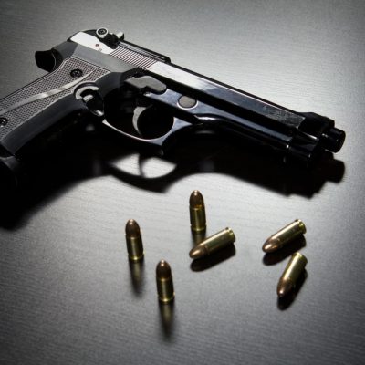 A black gun with five bullets sitting on a surface.