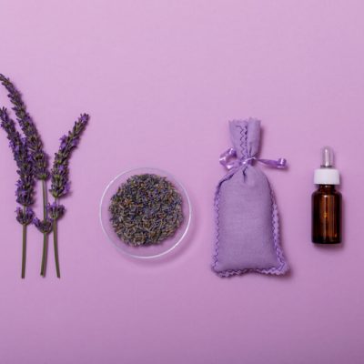 Essential lavender oil and flower with small bag on purpule background. Wellness with lavender, minimal concept. Beauty treatment top view.