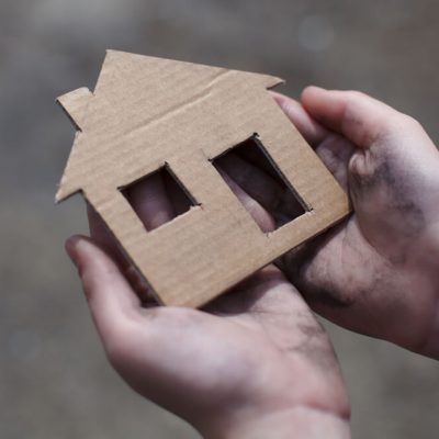 A homeless youth holding a cardboard house with a cut-out window and door.