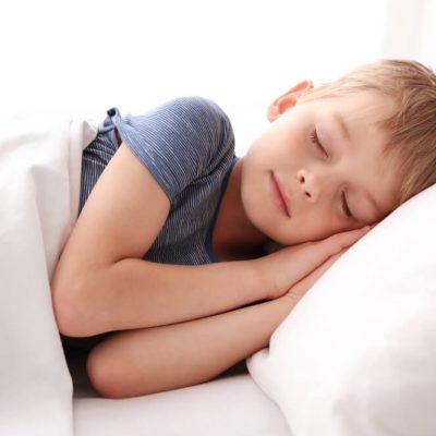 A child in a blue shirt sleeping on a white pillow with a white blanket.