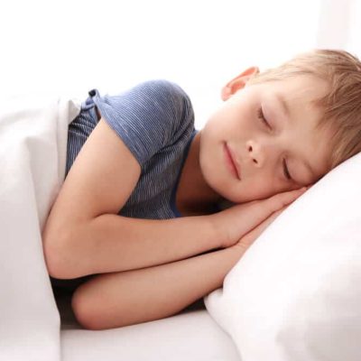 A child in a blue shirt sleeping on a white pillow with a white blanket.